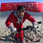 Michael Wigge am Strand vor einem "Start"-Schild - am nördlichsten Punkt Deutschlands, dem Ellenbogen auf der Nordseeinsel Sylt