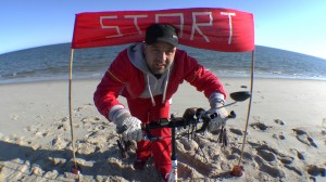 Michael Wigge am Strand vor einem "Start"-Schild - am nördlichsten Punkt Deutschlands, dem Ellenbogen auf der Nordseeinsel Sylt