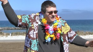 ein junger Mann mit Hawaiihemd und Kunstblüten-Kette tanzt Samba