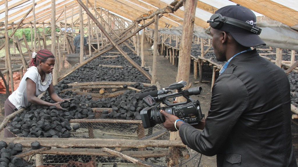 Camera man trains a camera on a woman drying briquettes in a shed