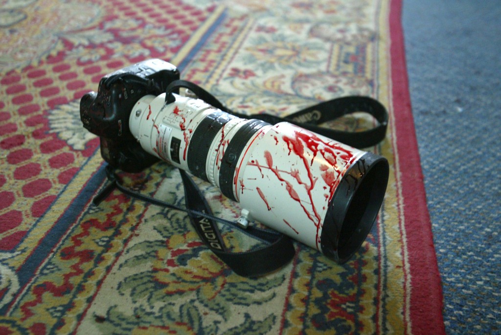 A camera covered with blood lies on a carpet