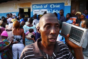 Man holds radio set to his ear in front of a polling station in Sierra Leone