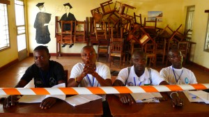 Four men sit in a row with notepads in front of them