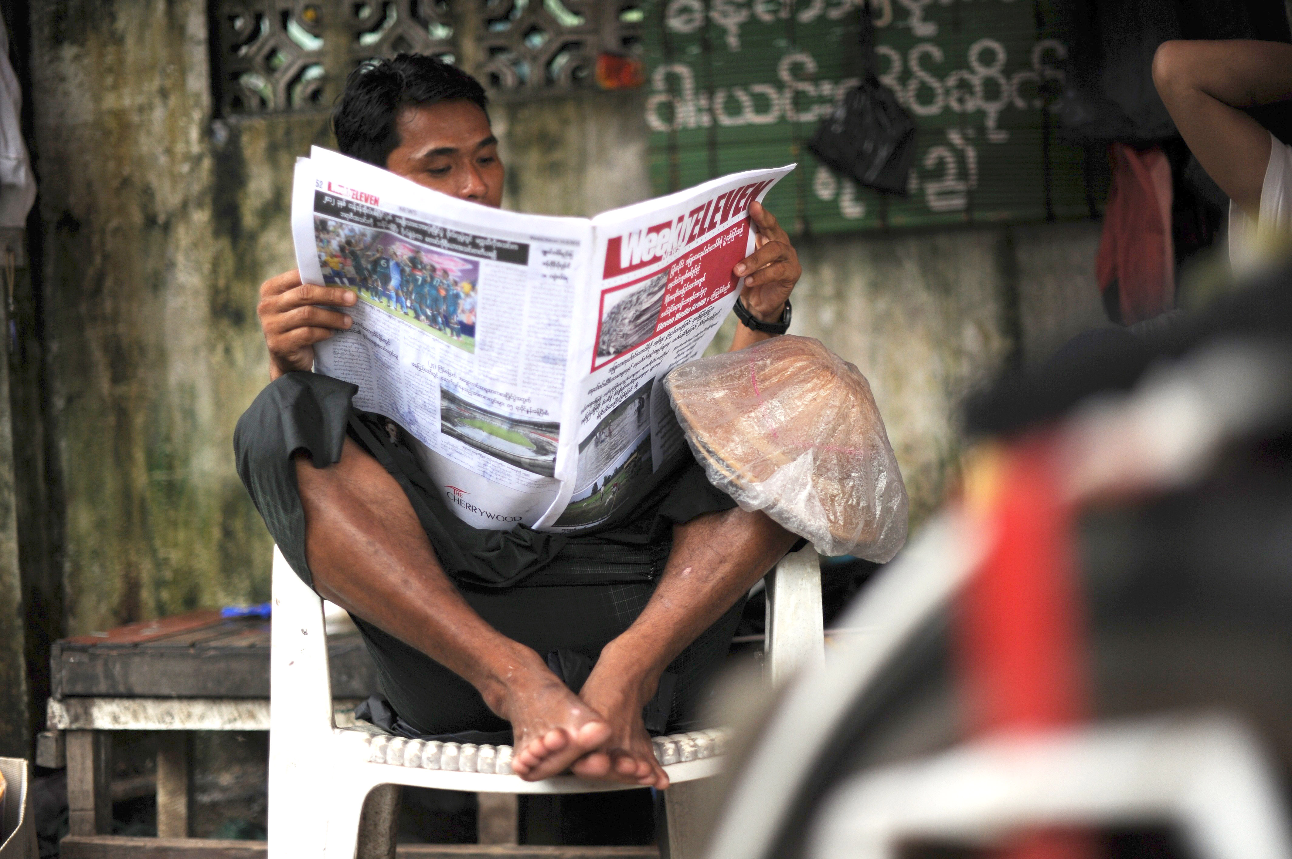 A man sitting in a chair reads a newspaper in Myanmar