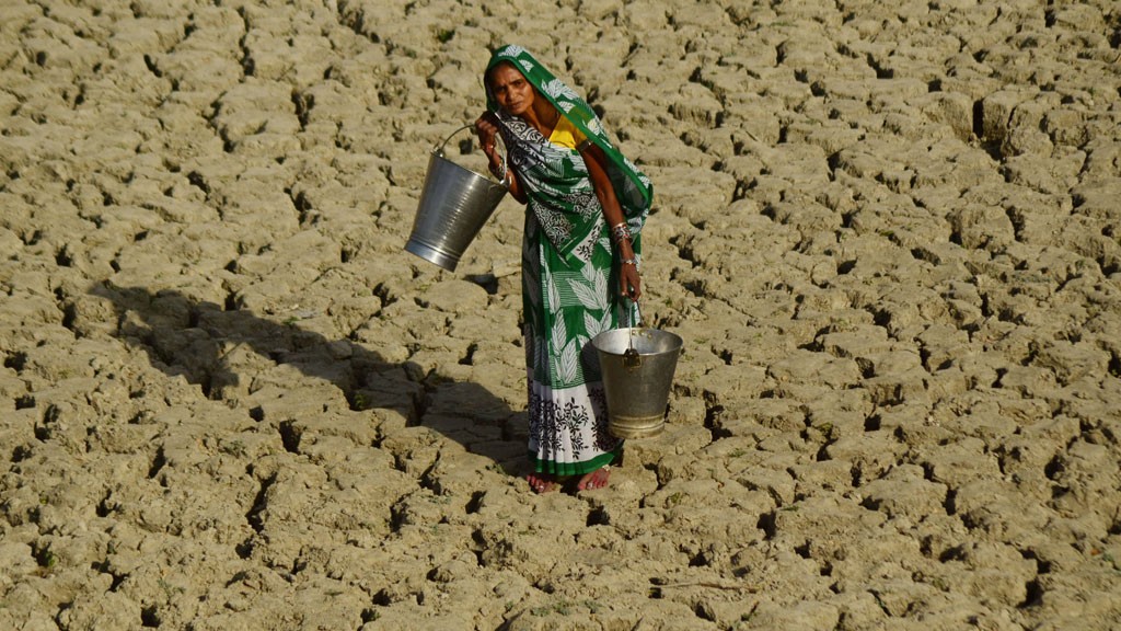 An indian woman walks on a dried and cracked water pond as she carries bucket to take drinking water. © Imago/Zuma Press 
